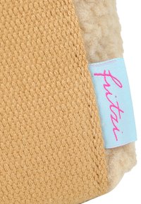 Tejido de color beige suave y esponjoso, con una textura tejida en tono marrón claro, que presenta una etiqueta azul clara con texto rosa cosida en el borde.