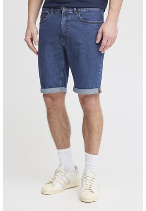 Shorts en denim bleu foncé avec un ourlet retroussé ; dotés de cinq poches, d'une fermeture à bouton et de coutures contrastantes. Assortis à des baskets blanches.