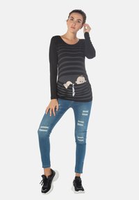 Schwarzes Langarmoberteil mit horizontalen Streifen, das ein Grafik von einem Baby zeigt; kombiniert mit zerstörten blauen Jeans und schwarzen Sneakers.