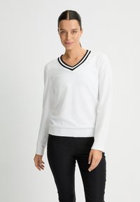 Weißer V-Ausschnitt-Pullover mit schwarzem Streifenbesatz, langen �Ärmeln, gerippten Bündchen und Saum; glatte Struktur; kombiniert mit schwarzen Hosen.