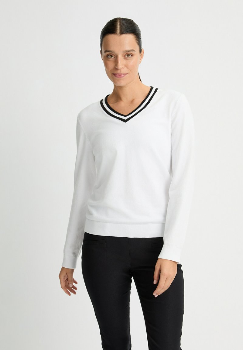 Suéter blanco de cuello en V con ribete a rayas negras, mangas largas, puños y dobladillo acanalados; textura suave; combinado con pantalones negros.