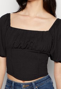 Svart kort topp med fyrkantig halsringning och puffärmar. Tillverkad av texturerat tyg med samlade detaljer och en figurnära design.