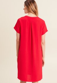Rotes Kurzarmkleid mit entspanntem Schnitt, mit rundem Ausschnitt und vertikaler Faltenpartie auf der Rückseite. Weicher, strukturierter Stoff.