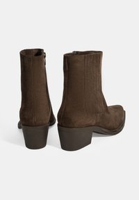 Bottines en suède marron avec un talon bloc, dotées d'une fermeture éclair et de coutures verticales sur les côtés pour ajouter de la texture.