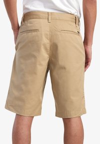 Beige shorts lavet af en blanding af bomuldsstof. Har to baglommer og en lige kant, designet til afslappet brug.