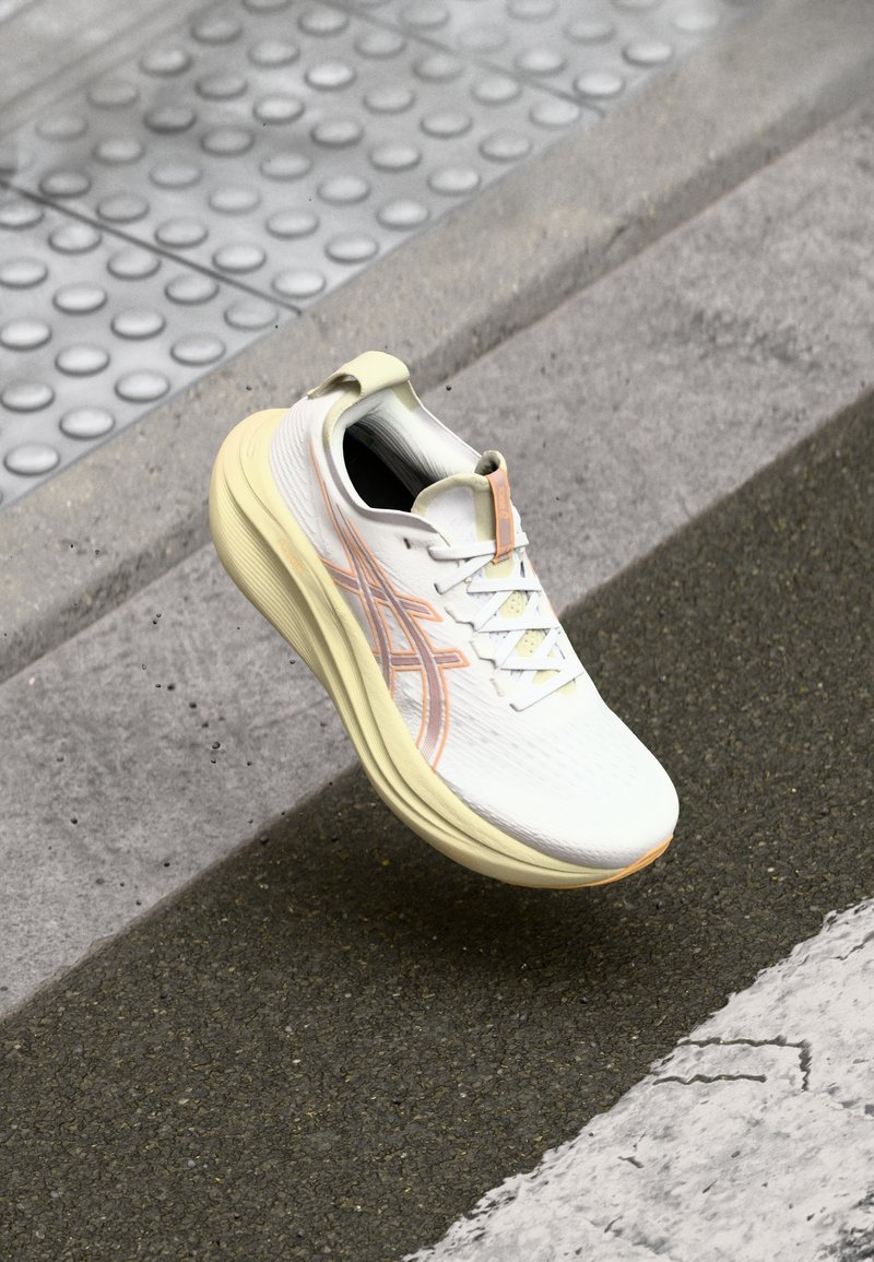Chaussure de course blanche et pêche clair flottant au-dessus d'un bord de trottoir texturé et d'une route asphaltée foncée avec une ligne blanche peinte.