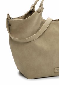 Beżowa zamszowa torba na ramię z pojedynczym szerokim paskiem, zaokrąglonym dnem i małą metalową metką marki blisko podstawy.