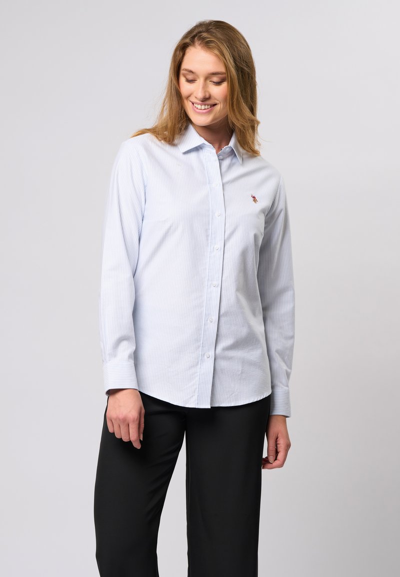 Hele sinine nööbitava särk, millel on õhukesed valged triibud, kaelusega disain ja väike logo aktsent rinnal. Pika varrukaga, sirgete mansettidega.