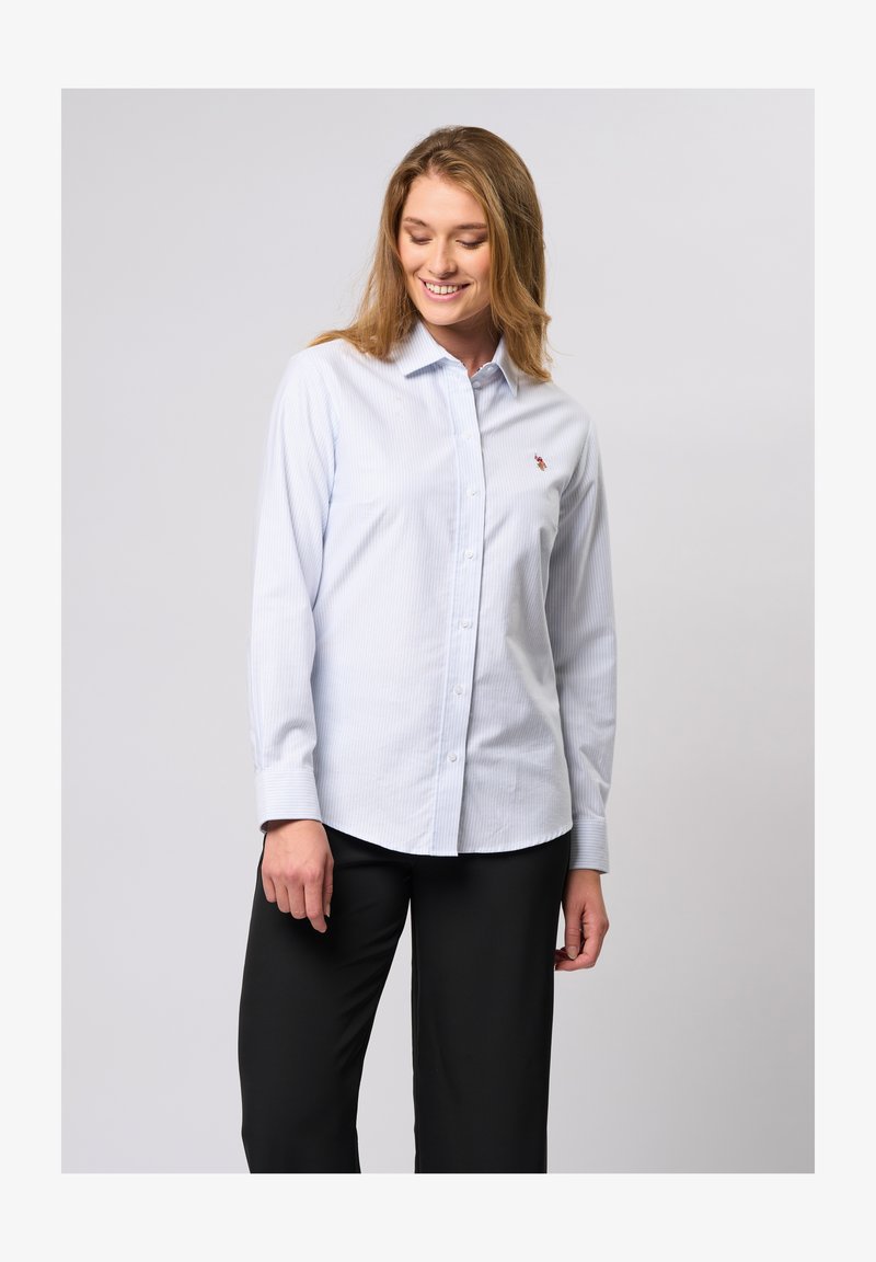 Jasnoniebieska koszula z długim rękawem, w cienkie białe paski, z kołnierzykiem i małym logo na piersi. Proste mankiety.