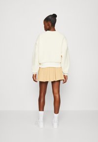 Pullover crema e soffice con design corto, abbinato a una gonna plissettata di un beige chiaro. Il modello indossa scarpe da ginnastica bianche e calze a crew.