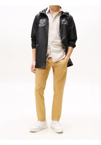 Czarna lekka kurtka, beżowa koszula w paski, jasnobrązowe spodnie i białe trampki. Kurtka posiada elastyczne mankiety i detale z logo.