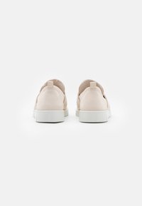Zapatillas de deporte rosa claro con una textura suave, suelas blancas planas y una lengüeta trasera. Presenta un diseño minimalista sin patrones visibles.
