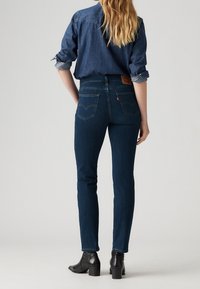 Mörkblå denimjeans med hög midja och slim fit. Har klassiska bakfickor och en läderlogotyp vid midjan. Svarta ankelboots.