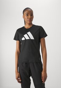 Must svart spordit-särk lühikeste varrukatega, ümmarguse kaelusega, millel on rinna peal suur valge Adidas'i logo, valmistatud sileda ja venivast materjalist.