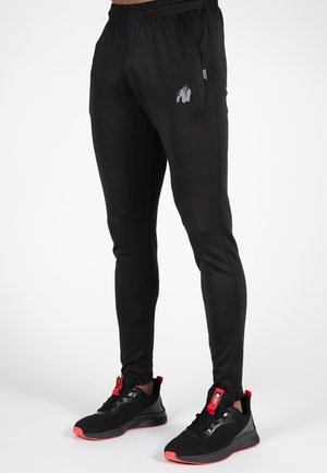 Pantaloni sportivi neri con vestibilità slim, vita elastica, tasca laterale e logo di un gorilla grigio sulla coscia sinistra.