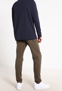 Mörkblå långärmad skjorta med avslappnad passform, ihop med olivgröna slim-fit-byxor. Vita sneakers fullbordar outfiten.