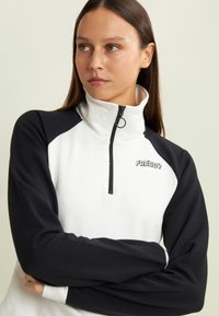 Sudadera en blanco y negro con cremallera de cuarto, mangas largas negras, tela suave y un logo plateado "FREDDY" en el pecho.