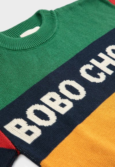 Sweter robiony na drutach z poziomymi paskami w kolorze zielonym, granatowym, czerwonym i żółtym. Napis "BOBO CHO" dużymi białymi literami na granatowej części.