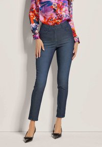Donkerblauwe denim jeans met een slim fit, voorzien van voorzakken, een knoopsluiting, en gecombineerd met een blouse met bloemenpatroon en zwarte hakken.