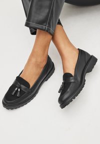 Czarne mokasyny zamszowe z przodu z ozdobami w formie frędzli, gumową podeszwą i wytrzymałą konstrukcją. Gładka skóra i teksturowane materiały wierzchnie.