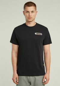 T-shirt en coton noir avec un col ras du cou et un logo Q-STAR brodé sur la poitrine gauche. Manches courtes et ourlet droit.