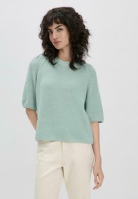 Pull en maille vert menthe avec des manches raglan courtes et un col rond, présentant un motif texturé et une coupe décontractée.