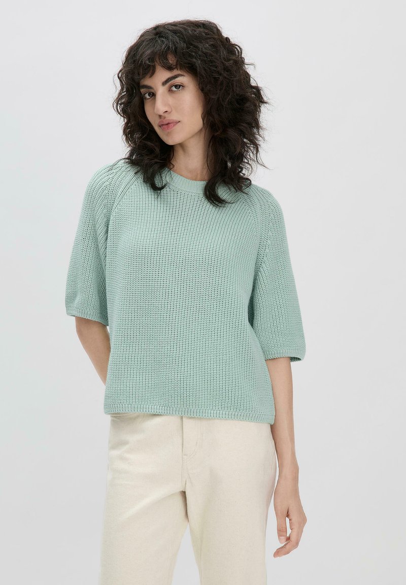 Pull en maille vert menthe avec des manches raglan courtes et un col rond, présentant un motif texturé et une coupe décontractée.