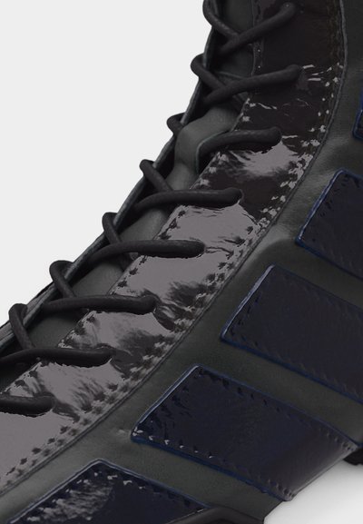 Κοντινό πλάνο μαύρου παπουτσιού με γυαλιστερό πάνελ από πατενταρισμένο δέρμα στα κορδόνια, μαύρα κορδόνια και σκουρό μπλε υφασμάτινες ρίγες στο πλάι.