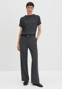 Haut texturé noir à manches courtes, associé à un pantalon large taille haute. Une ceinture noire et des chaussures plates complètent le look.