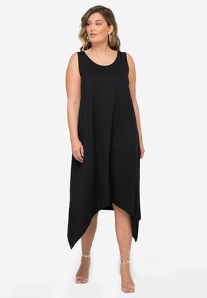 Abito nero senza maniche con scollo rotondo, orlo asimmetrico e tessuto morbido e leggero. La modella sta in posa con visibilità chiara delle caratteristiche del design.