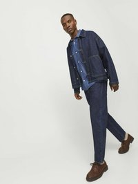 Jachetă din denim și pantaloni de culoare albastru închis, cu o cămașă albastră deschisă dedesubt; pantofi maro; croi lejer și design clasic cu buzunare.
