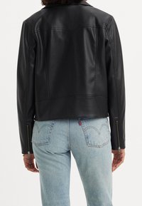 Czarna skórzana kurtka o krótkim kroju, gładkiej fakturze i widocznych przeszyciach; posiada suwaki na mankietach rękawów. Połączona z jasnoniebieskimi dżinsami.