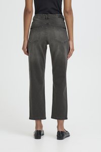 Osoba ubrana w ciemnoszare dżinsy z wysokim stanem i prostymi nogawkami oraz czarne mokasyny, stojąca tyłem do kamery na białym tle.