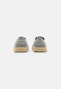 Baskets slip-on en toile grise avec semelle en jute, arborant un logo à l'arrière. Design minimaliste avec des accents élastiques sur les côtés pour un enfilage facile.