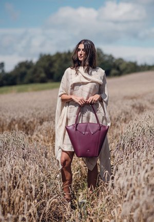 Lila Leder-Taschen mit einer einzigartigen Form, die dreieckige Akzente und silberne Hardware aufweist, wird von einer Person in einem strukturierten beigen Outfit gehalten.