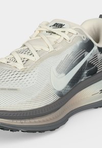 Λευκό και γκρι αθλητικό παπούτσι Nike για τρέξιμο με επάνω μέρος από δίχτυ, λευκά κορδόνια και μαλακή σόλα, με μεγάλο λογότυπο Swoosh στο πλάι.