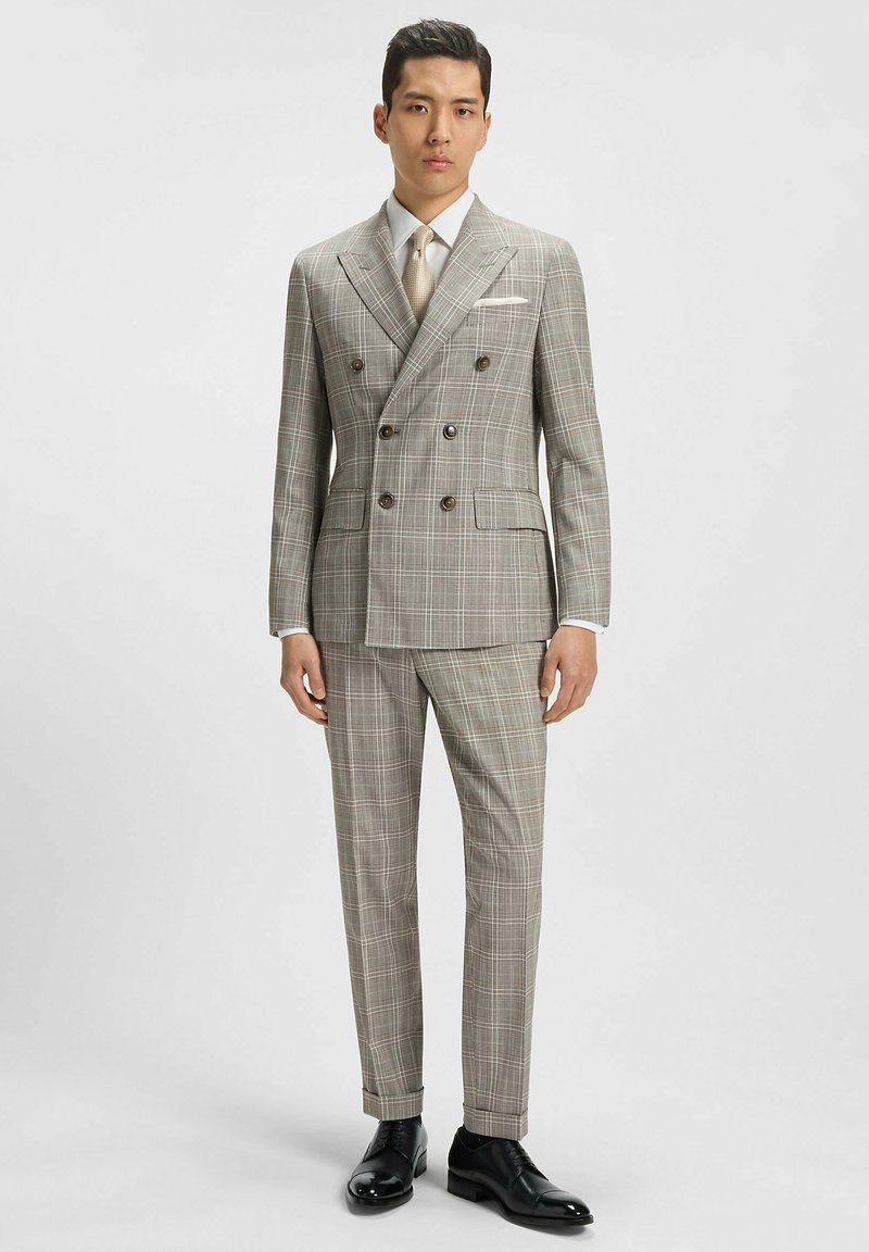 Double-breasted suit in light gray with a plaid pattern, matching trousers, and a white shirt. Black dress shoes complete the look.
