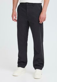 Black cotton trousers with a straight fit, featuring a button closure and front pockets, paired with white sneakers. Simple, classic design.