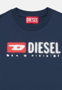 Tamnoplava majica kratkih rukava s okruglim izrezom. Na prednjoj strani istaknut je bijeli i crveni Diesel logo s grafičkim dizajnom i teksturalnim varijacijama.