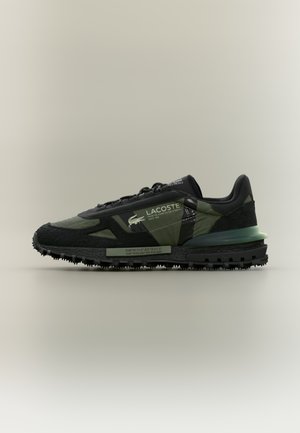 Black and green sneaker with mesh and suede materials, padded collar, textured rubber sole, and contrasting reflective accents.