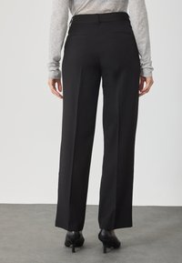 Calças altas pretas com um design de perna reta, apresentando bolsos traseiros e uma textura subtil. Usadas com saltos altos pretos.