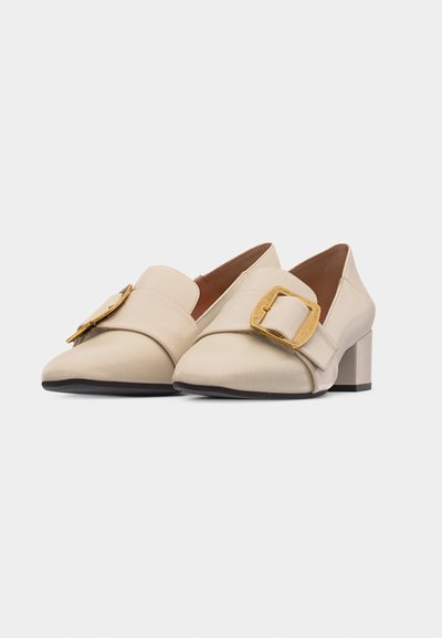 Mocassins à talons pour femmes de couleur crème avec de grandes boucles carrées dorées et un design à bout arrondi sur un fond uni.