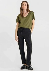 Olivengroen T-shirt met V-hals gecombineerd met zwarte pantalon met krijtstrepen. De pantalon heeft een taille met trekkoord en zijzakken, gemaakt van een gestructureerde stof.