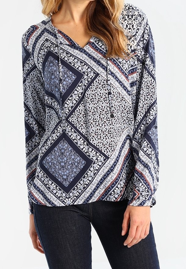 Blouse bleu marine à motifs floraux et géométriques, manches longues, encolure en V et cordons avec accents décoratifs.