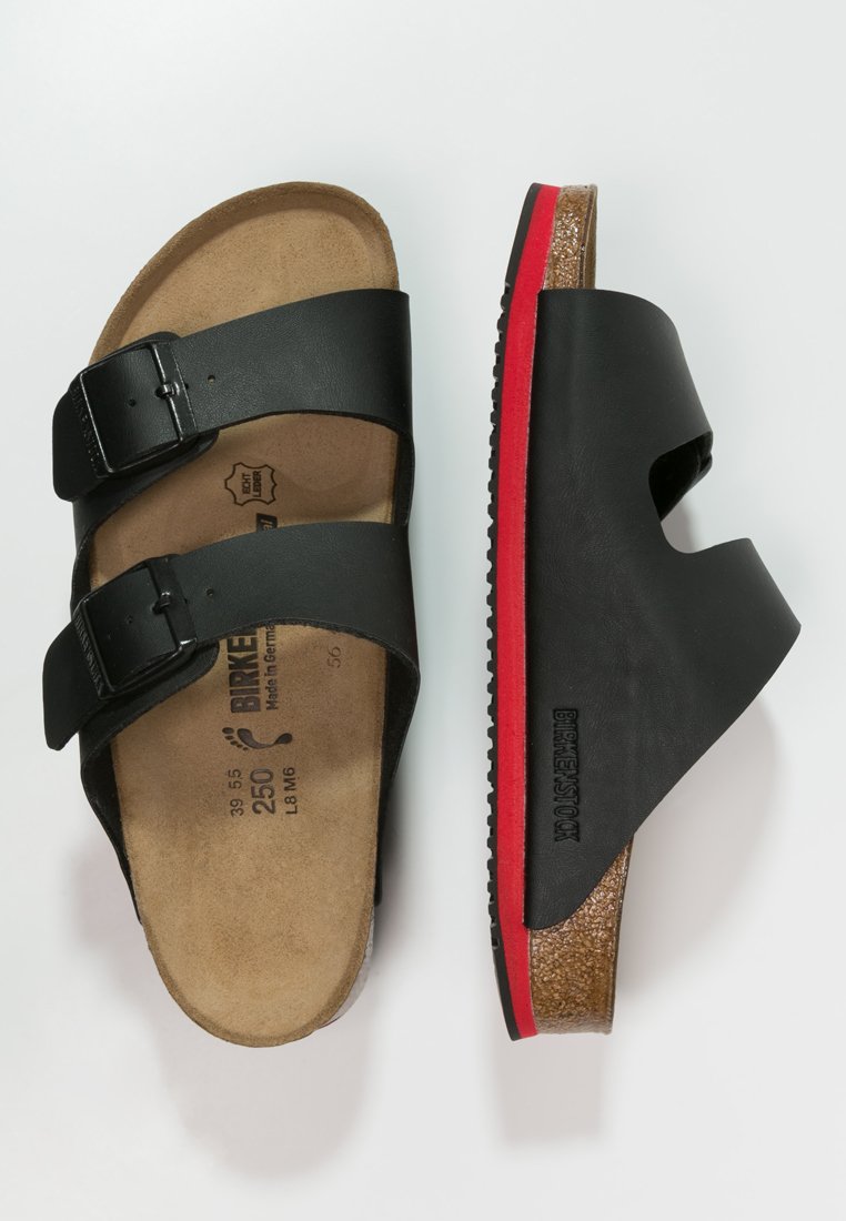 Black sandals featuring two adjustable straps, cork footbed, and a textured rubber sole with a red accent along the edge.