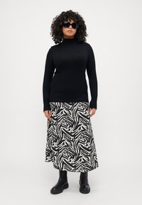 Svart turtleneck-genser kombinert med et langt svart og hvitt zebra-mønstret skjørt. Modellen har på seg svarte oversized solbriller og svarte støvler.