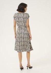 Robe à motifs noir et crème avec des manches courtes, taille cintrée et jupe évasée. Portée avec des sandales à talons noires.