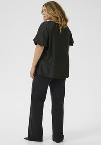 Schwarzes, strukturiertes Oberteil mit Puffärmeln und einer Schlitzdetail am Rücken, kombiniert mit schwarzen weiten Hosen, die eine entspannte Silhouette schaffen.