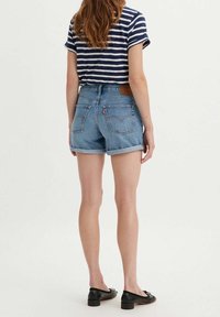 Pantalones cortos de mezclilla de tiro alto, color azul claro desteñido, dobladillos enrollados y bolsillos traseros. Camiseta de rayas azul marino y blanca, llevada por encima.