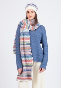 Blå strikket sweater med struktureret mønster, parret med et mønstret tørklæde i pastelfarver og en matchende cremet hue.